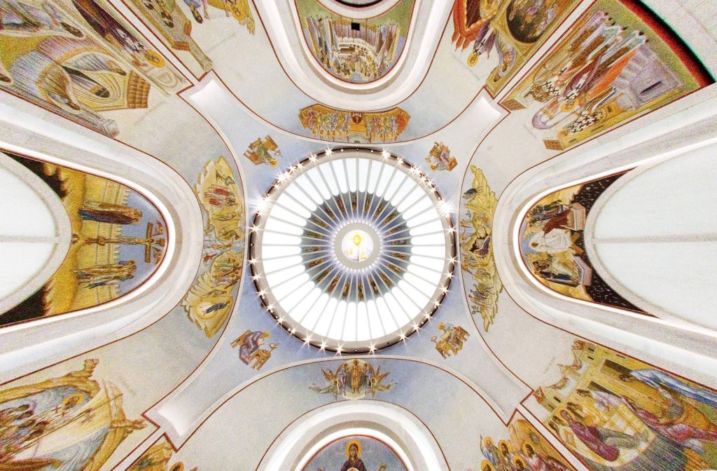 Dome view of inside of St. Nicholas Greek Orthodox Church & National Shrine with white marble and murals along the ceiling walls